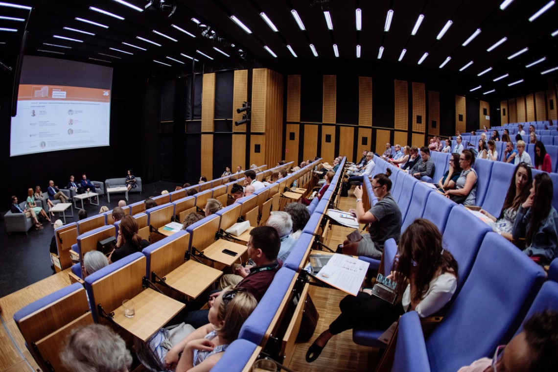 Sala wykładowa. Ludzie słuchają siedzących na dole panelistów